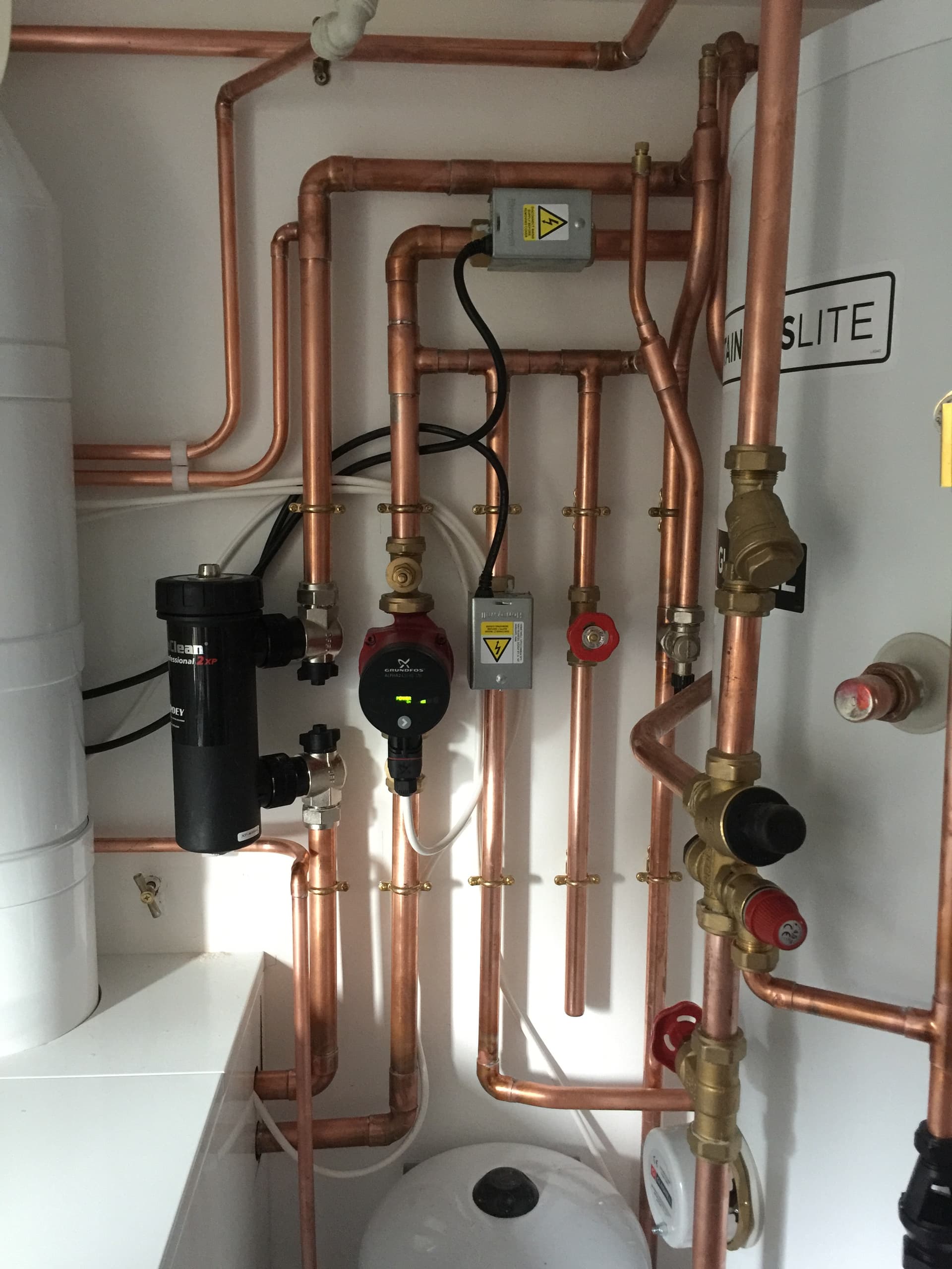 Exposed copper pipework, isolation valves and connected controls inside a service cupboard.