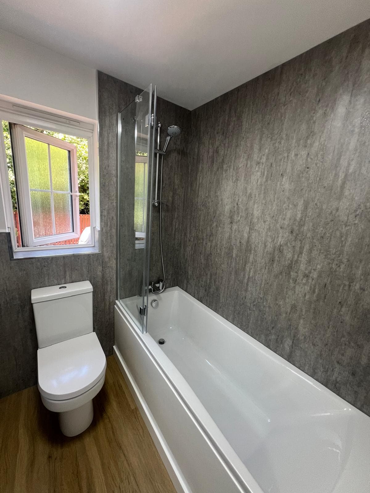 Bath with shower screen and grey stone-effect wall panels, fitted by Truscon