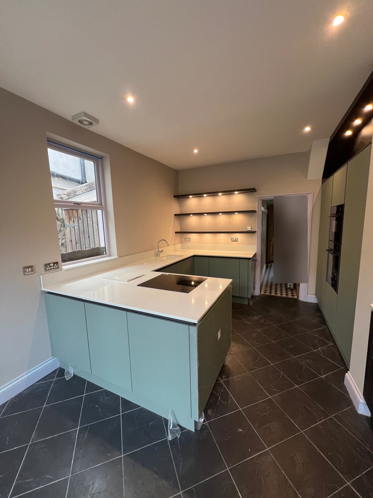 Sage green island with quartz worktop and lit floating shelves, fitted by Truscon